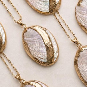 May include: Several oval-shaped pendants featuring iridescent abalone shell centres framed by textured gold-tone metal edges. Each pendant is attached to a delicate gold-tone metal chain, showcasing a natural pearlescent finish with pink and green hues.