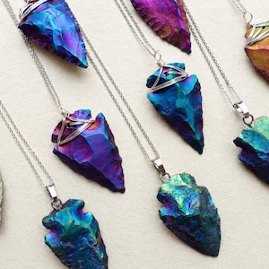 May include: A collection of necklaces featuring iridescent arrowhead-shaped pendants in shades of blue, purple, green, and gold. Each pendant is secured with silver-toned wire wrapping and hangs from a delicate silver-toned metal chain.