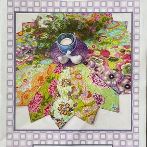 May include: A quilt pattern titled "Lazy Daisy" with a floral design. The pattern is 42 inches in diameter and features a variety of colorful flowers in shades of pink, green, and orange. The image also includes a candle, decorative birds, and text that reads "Sewn into the fabric... Pieces of our lives."