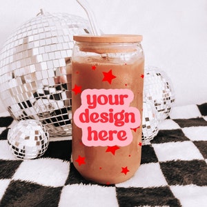 May include: A glass jar with a wooden lid filled with a brown liquid. The jar has a pink sticker with the text "your design here" and red stars. The jar is sitting on a black and white checkered surface.