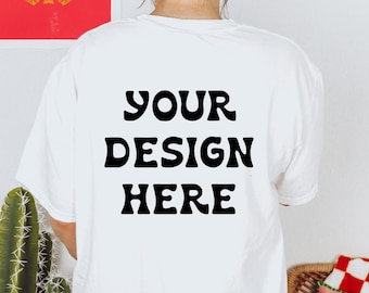 Può includere: Maglietta bianca con il testo "YOUR DESIGN HERE" stampato in nero sul retro.