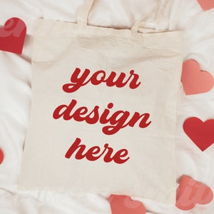 May include: A white tote bag with red text that says "your design here" on a white background. The bag is surrounded by pink and red hearts.