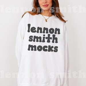 Może przedstawiać: Biała bluza z czarnym napisem "lennon smith mocks" w retro czcionce.