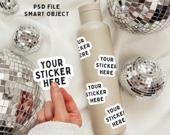 May include: A beige reusable water bottle with a white sticker that says "YOUR STICKER HERE". The bottle is surrounded by silver disco balls on a white background.
