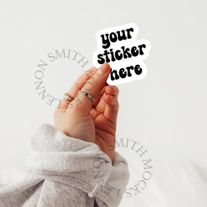 May include: A white sticker with black text that reads "your sticker here" in a retro font. The sticker is being held by a hand.