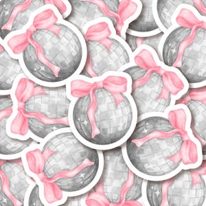 K&ouml;nnte beinhalten: Eine Bogen mit Aufklebern mit rosa Schleifen und silbernen Discokugeln. Jeder Aufkleber hat einen wei&szlig;en Rand.