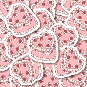 K&ouml;nnte beinhalten: Ein Muster aus rosa herzf&ouml;rmigen Kuchen mit wei&szlig;em Frosting und roten Kirschen. Die Kuchen sind in einem sich wiederholenden Muster angeordnet.