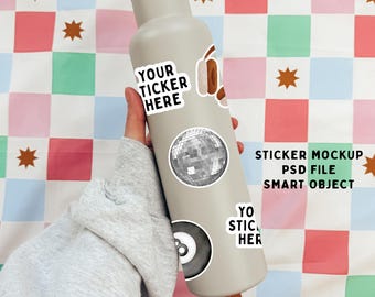 May include: A grey water bottle with a variety of stickers, including a disco ball, a pair of headphones, and a pool ball. The text "YOUR TICKER HERE" is on one of the stickers. The text "STICKER MOCKUP PSD FILE SMART OBJECT" is also on the bottle. The bottle is being held by a hand.