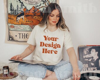 May include: A woman wearing a white t-shirt with the text "Your Design Here" in orange. She is sitting on a white rug with a vintage tapestry and a record player behind her.