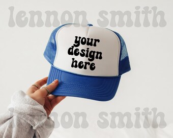 Könnte beinhalten: Eine weiße und blaue Trucker-Kappe mit einem blauen Netzrücken. Die Vorderseite der Kappe hat schwarzen Text, der in einer Retro-Schrift "your design here" lautet.