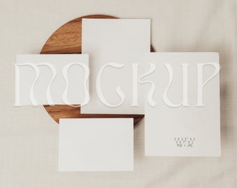 May include: Three blank white cards on a wooden surface. The cards are different sizes and are arranged in a staggered pattern. The text "MOCKUP" is written in white on the cards. The text "5 x 3.5" x 2, 5 x 7" x 2, PSD + JPG" is written in gray on the bottom right card.