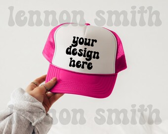 Könnte beinhalten: Eine weiße und rosafarbene Trucker-Kappe mit Netzrücken. Die Vorderseite der Kappe hat schwarzen Text mit der Aufschrift "your design here".