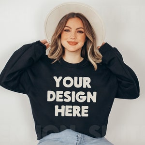May include: A black sweatshirt with the text "YOUR DESIGN HERE" in white. The sweatshirt is being modeled by a person wearing a white hat and blue jeans.