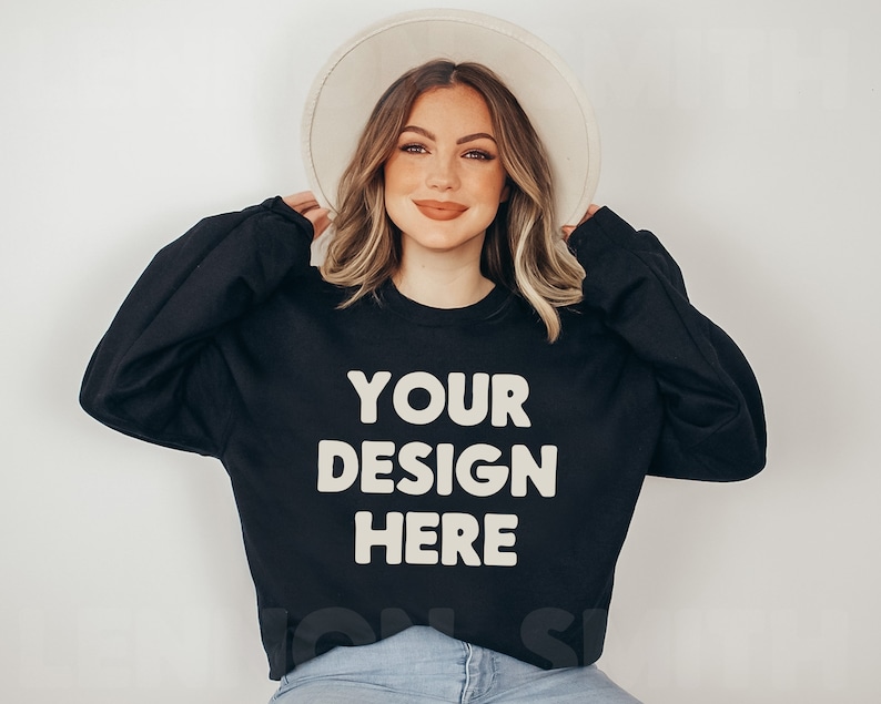 May include: A black sweatshirt with the text "YOUR DESIGN HERE" in white. The sweatshirt is being modeled by a person wearing a white hat and blue jeans.