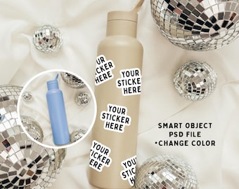 May include: A beige water bottle with a silver lid and a silver cap. The bottle has five white stickers with black text that says "Your Sticker Here". The bottle is surrounded by silver disco balls on a white fabric background.