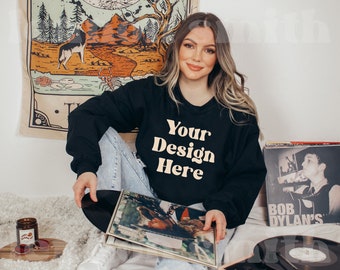 May include: A black sweatshirt with the text "Your Design Here" in a cream colour. The sweatshirt is being worn by a person sitting on a white fluffy surface. The person is holding a black vinyl record.