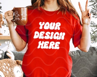 Può includere: Una maglietta rossa con il testo "YOUR DESIGN HERE" in bianco, con caratteri in stile retrò. La maglietta è indossata da una persona con i capelli lunghi e castani.