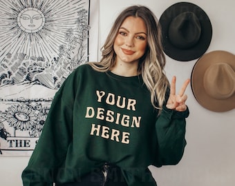 May include: A dark green sweatshirt with the text "YOUR DESIGN HERE" in a light yellow color. The sweatshirt is being worn by a person with long brown hair.