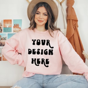 May include: A pink sweatshirt with the text "YOUR DESIGN HERE" in black, retro-style lettering.
