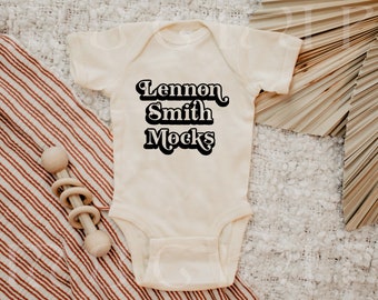 May include: A white baby onesie with black text that reads "Lennon Smith Rocks".