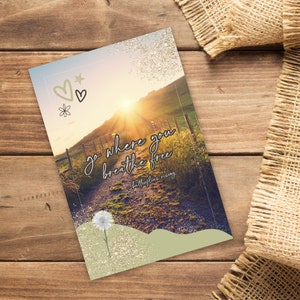May include: A greeting card with a scenic landscape featuring a path leading towards a bright sunset. The card has the text "go where you breathe free" and "butterflies rising". Decorative hearts, stars, and a flower are in the upper left corner.