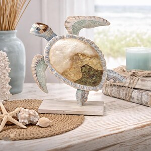 May include: A decorative turtle figurine with a light blue, beige, and brown color scheme. The turtle has detailed patterns on its shell and flippers, and it stands on a small wooden base. The figurine is a coastal-themed home decor item.