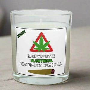 Peut inclure: Une bougie en verre transparent avec une étiquette blanche représentant une feuille de cannabis verte à l'intérieur d'un triangle rouge, et le texte "SORRY FOR THE BLUNTNESS. THAT'S JUST HOW I ROLL." Le mot "JONNY" est en vert en haut.