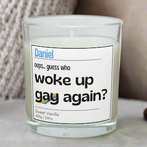 May include: A glass candle with a white label. The label reads "Daniel, oops.. guess who woke up gay again?" with a rainbow flag. It is labeled "Sweet Vanilla, 420g | 25hrs."
