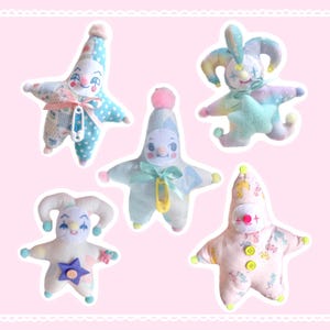 Könnte beinhalten: Fünf sternförmige Plüschpuppen mit clownartigen Gesichtern und verschiedenen Pastellfarben. Jede Puppe hat ein einzigartiges Design, einschließlich Tupfen, Schleifen und Sternakzenten. Die Puppen sind vor einem rosa Hintergrund platziert.