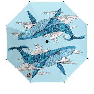 Puede incluir: Un paraguas azul con un diseño de dos ballenas azules nadando en las nubes. Las ballenas están detalladas con intrincados patrones.