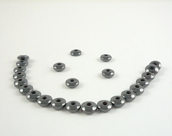 May include: A smiley face made of dark gray beads. The beads are arranged in a semi-circle with five beads forming the smile.