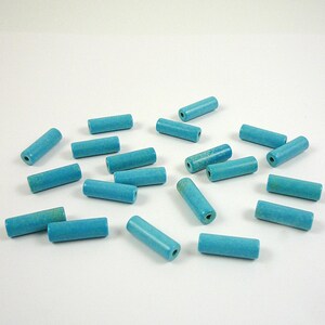May include: A collection of turquoise-colored, cylindrical beads scattered on a white surface. Each bead has a hole running through its center, and they vary slightly in shade, with some showing a hint of green. These beads are suitable for jewelry making.