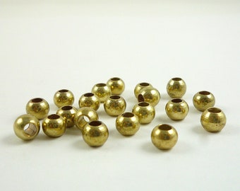 May include: A collection of small, round, brass-colored beads with a hole through the center. The beads are scattered across a white surface, showcasing their metallic sheen and simple design. Ideal for jewelry making or craft projects.