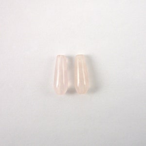 May include: Two teardrop-shaped rose quartz beads. The beads are a soft pink color and have a smooth, polished surface. They are displayed against a white background.