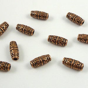 May include: Ten copper-colored metal beads with a geometric pattern. The beads are oval-shaped and have a slightly textured surface.