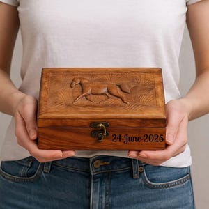 May include: Wooden box with a carved horse design on the lid. The box is rectangular with a hinged lid and a metal clasp. The date "24-June-2025" is engraved on the front.