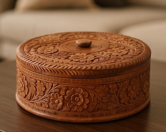 May include: A round, wooden box with intricate floral carvings. The box is a warm brown color and has a lid with a small, round knob. The detailed carvings cover the lid and sides, showcasing a handcrafted design. The box sits on a dark brown table.