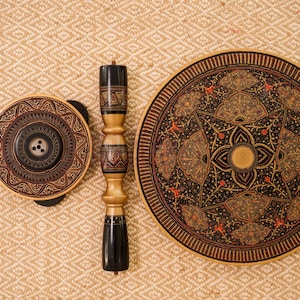May include: An overhead shot of a decorative wooden table and components. The table has a round top with intricate patterns in black, gold, and red. The components include a matching round piece and a central support column.