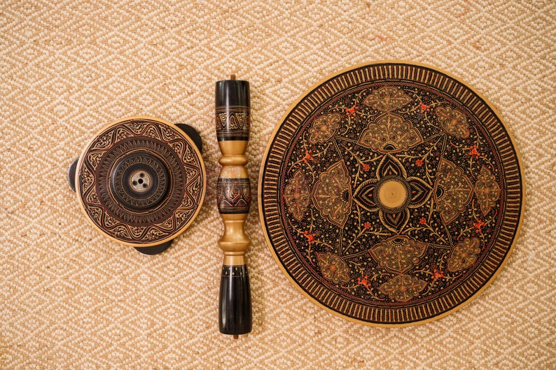 May include: An overhead shot of a decorative wooden table and components. The table has a round top with intricate patterns in black, gold, and red. The components include a matching round piece and a central support column.