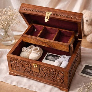 May include: A wooden keepsake box with a hinged lid, carved floral designs, and a brass clasp. Inside, a red velvet lining complements the box's contents: baby booties, ultrasound images, and small white items.