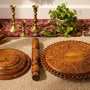May include: A collection of decorative items, including a carved wooden tray, a wooden elephant figurine, and brass candlesticks. The tray features intricate floral patterns. A small potted plant and a bundle of dried lavender are also present.