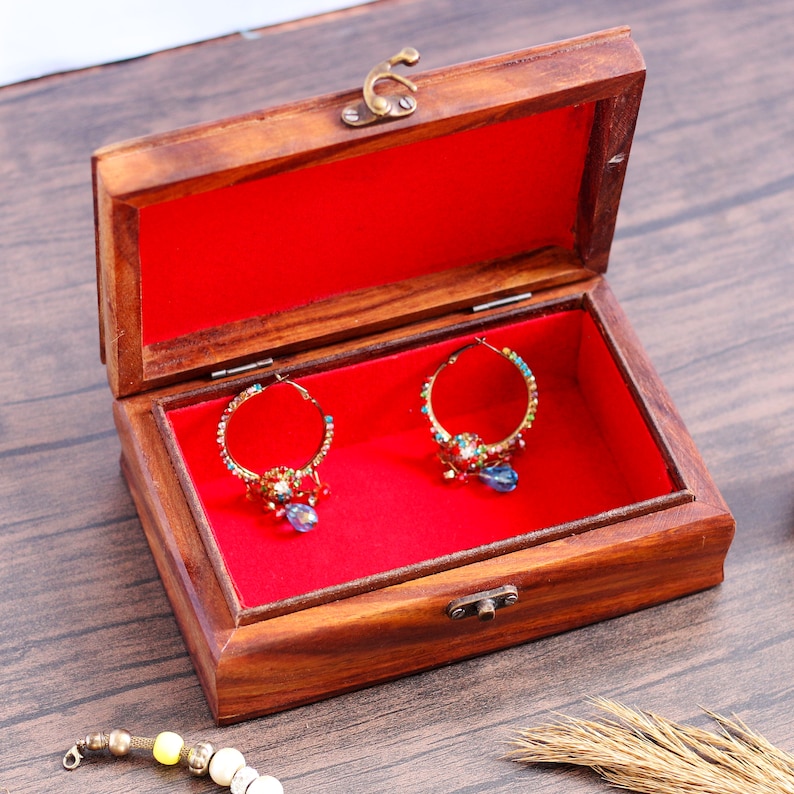 May include: A wooden jewelry box with a red velvet interior. The box is open and two pairs of gold hoop earrings with colorful stones are visible inside.