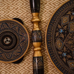 May include: A collection of decorative wooden items with intricate designs. The pieces include a round plate, a smaller circular object, and a central support column. The items feature black, gold, and blue accents, with detailed patterns.