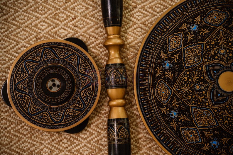 May include: A collection of decorative wooden items with intricate designs. The pieces include a round plate, a smaller circular object, and a central support column. The items feature black, gold, and blue accents, with detailed patterns.