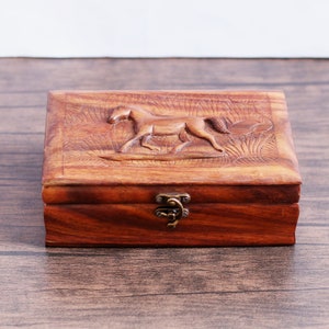 May include: A wooden box with a carved horse design on the lid. The box has a brass latch and is made of dark wood.