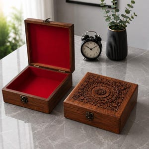 May include: Two wooden jewelry boxes. One box is open, revealing a red velvet interior. The other box is closed, with an intricate floral design carved into the lid. Both boxes have metal clasps.