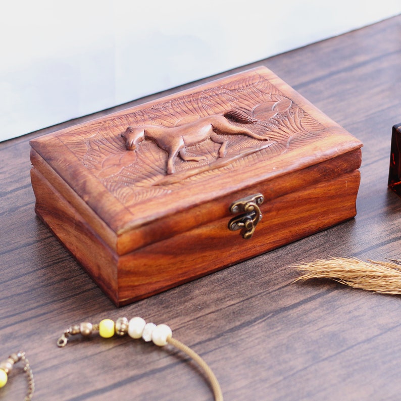 May include: A wooden box with a carved horse design on the lid. The box has a brass latch and is made of dark brown wood.