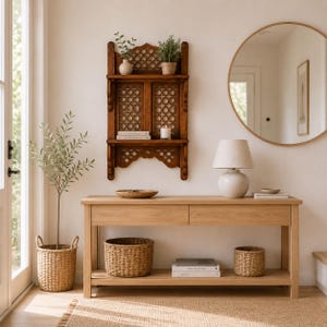 May include: A light oak console table with two drawers and a lower shelf, featuring two woven baskets and stacked books. Above it hangs a dark wood wall shelf with intricate lattice panels, holding two small potted plants and a candle.