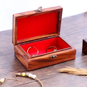 May include: A wooden jewelry box with a red velvet interior. The box is open and has a ring and earrings inside.