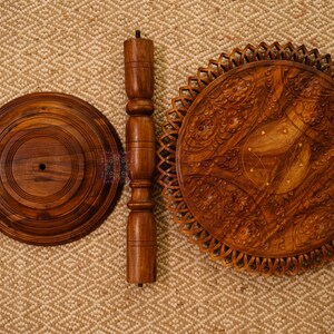 May include: A disassembled wooden side table with a round base, a central support, and a decorative tabletop. The tabletop features intricate carved floral patterns. The wood has a warm, brown tone.